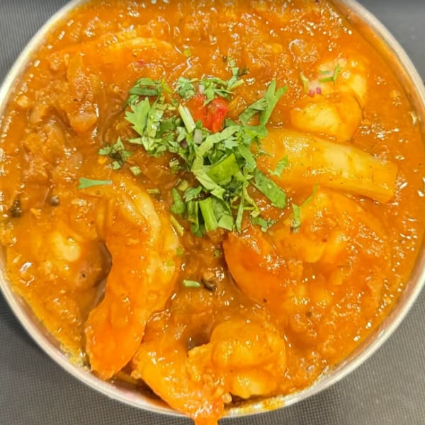 Shrimp curry with cilantro garnish in a traditional copper serving bowl.