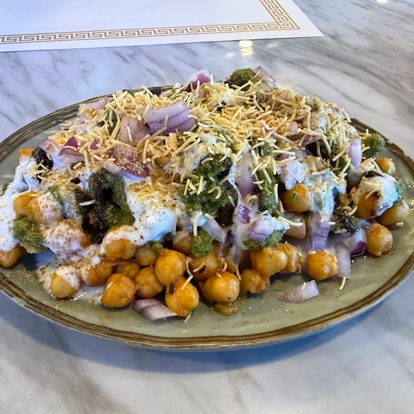 Chickpea chaat with green and white sauces, red onions, and crispy toppings on a green plate.