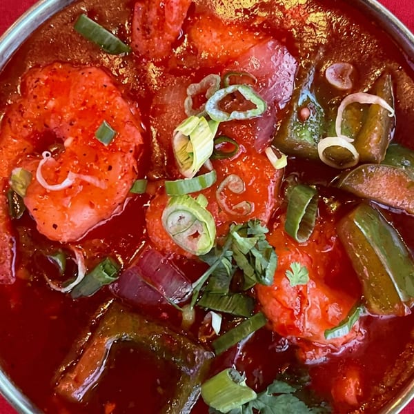 Vibrant red shrimp curry with sliced green onions and peppers in an ornate metal serving dish.