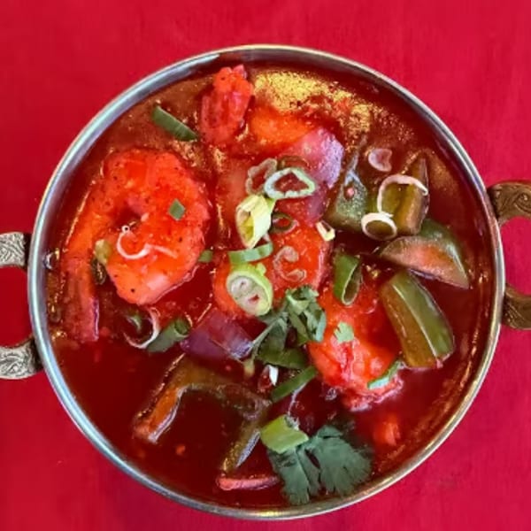 Vibrant red shrimp curry with green peppers and scallions in a decorative metal bowl.