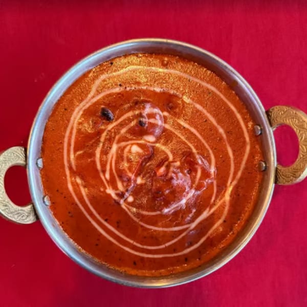 Rich orange curry with a swirl of cream in a brass-handled bowl on a red tablecloth.