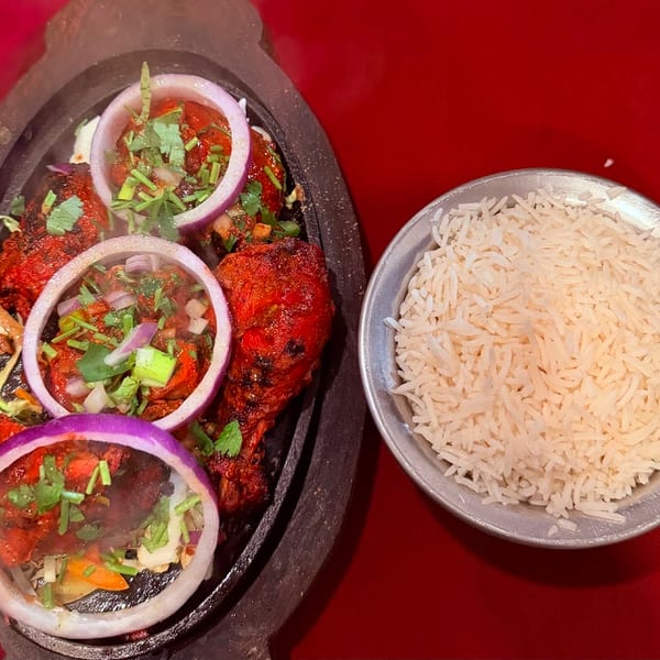 Sizzling tandoori chicken with red onions and herbs, served with a side of white rice.