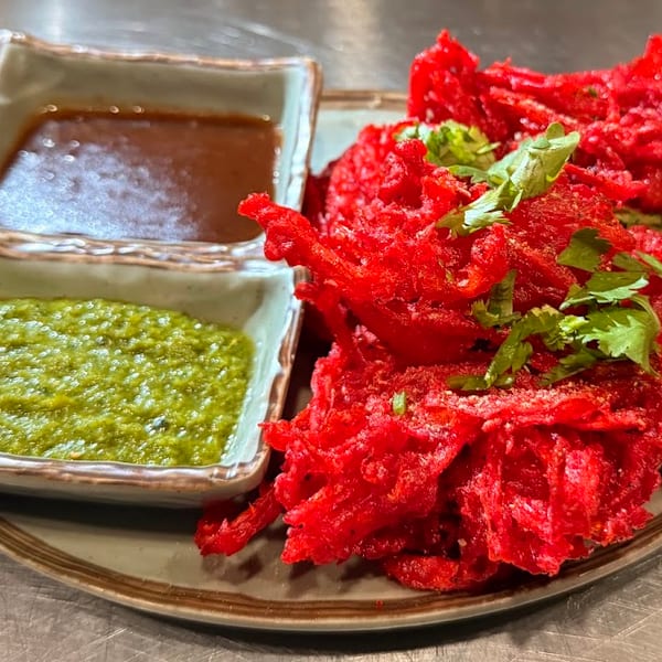 Vibrant red crispy fritters with cilantro, accompanied by green and brown dipping sauces.