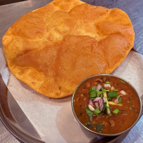 Puffy golden fried bread served with a bowl of chana masala, garnished with onions and ginger.