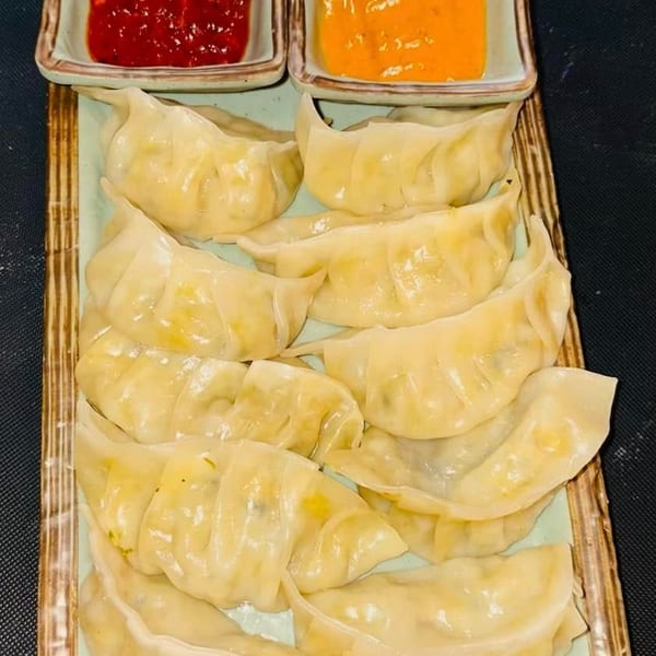 A platter of steamed dumplings, or momos, with two dipping sauces, one red and one orange.
