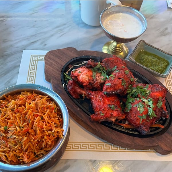 Tandoori chicken on a sizzling platter with biryani rice, green chutney, and raita.