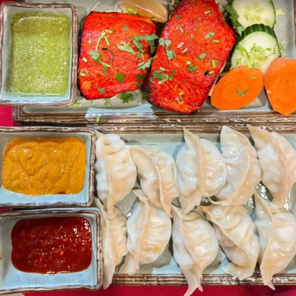 Two plates of food, one with red fish and vegetables, the other with dumplings and three sauces.