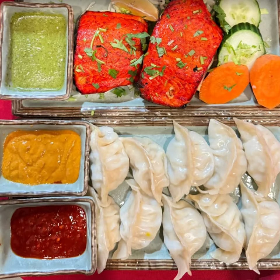 Two plates of food, one with red fish and vegetables, the other with dumplings and three sauces.