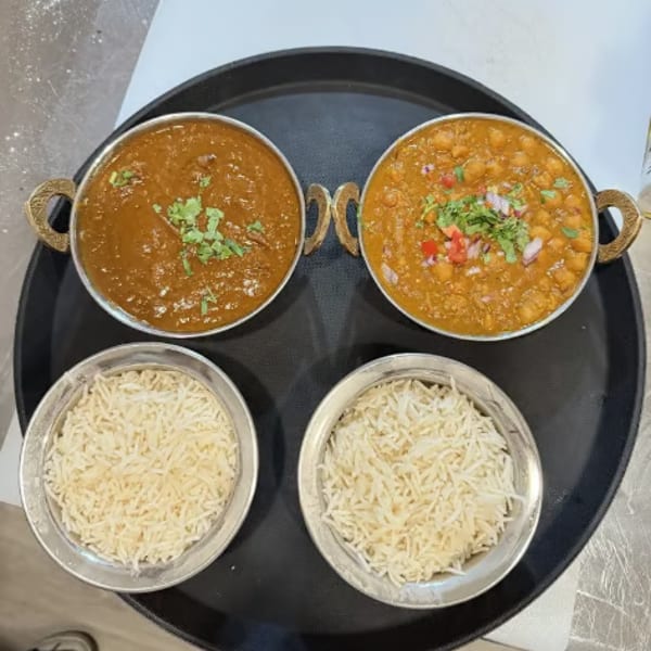 Two bowls of curry and two bowls of rice on a black serving tray.