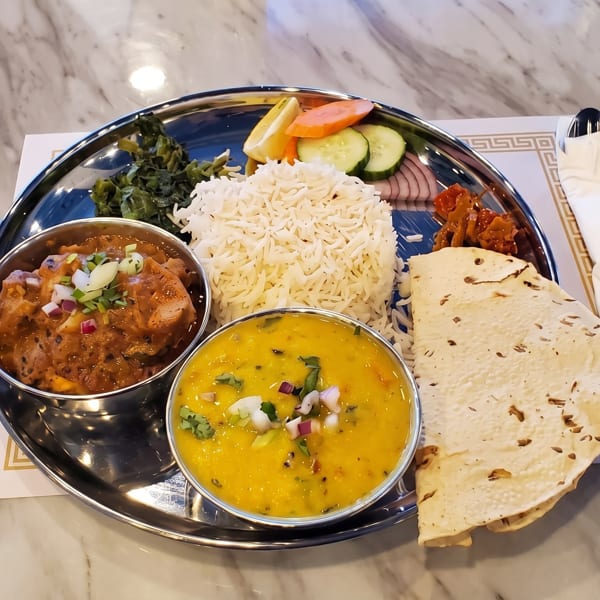 A metal platter holds a colorful Indian thali with rice, curries, vegetables, and flatbread.