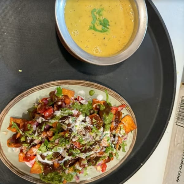 A plate of loaded sweet potato fries with sauces and a bowl of yellow lentil soup.