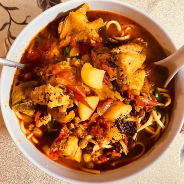 Spicy chicken noodle soup with potatoes, red peppers, and spices in a white bowl.