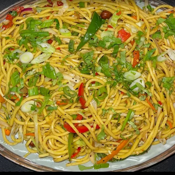 Close-up of a plate of vibrant stir-fried noodles with mixed vegetables and fresh herbs.
